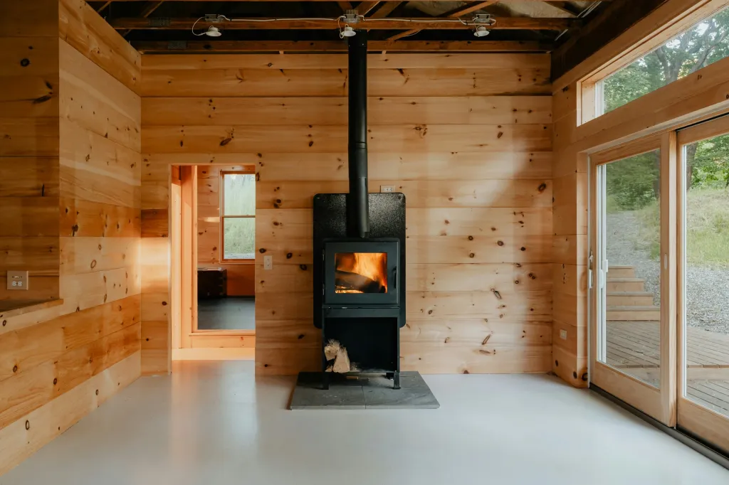 Holzverkleideter Raum mit schwarzem Kaminofen und Glasfront zum Garten