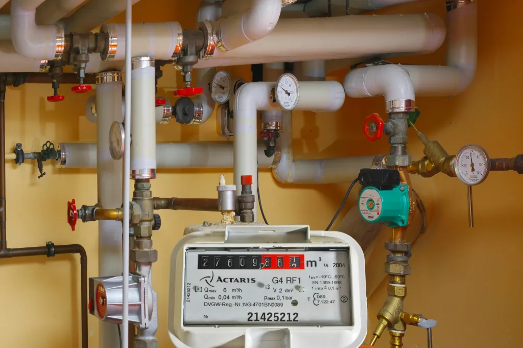 Actaris Gaszähler mit weißen Rohrleitungen, roten Ventilen und Manometern vor gelber Wand