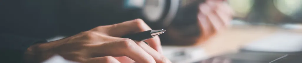 Hand hält Kugelschreiber über Dokumenten am Schreibtisch