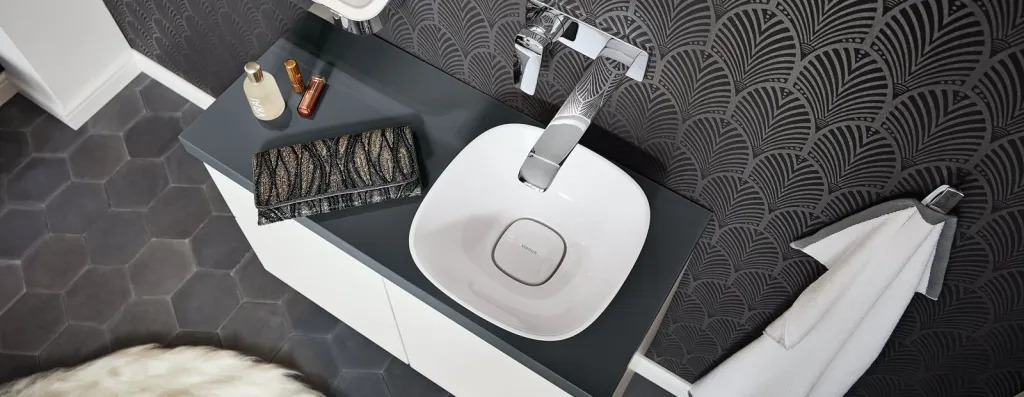 Vogelperspektive auf weißes Aufsatzwaschbecken mit Wandarmatur auf dunkler Waschtischplatte