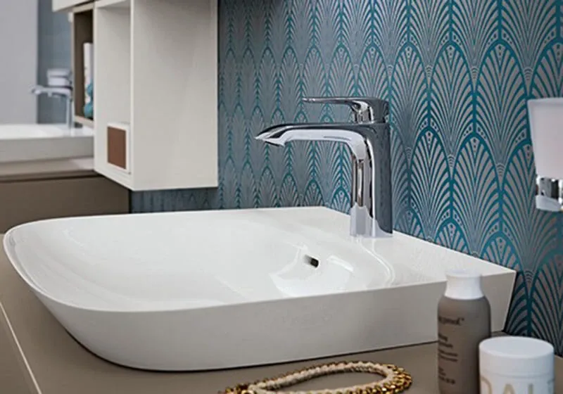 Weißes Aufsatzwaschbecken mit verchromter Armatur vor türkisfarbener Mustertapete