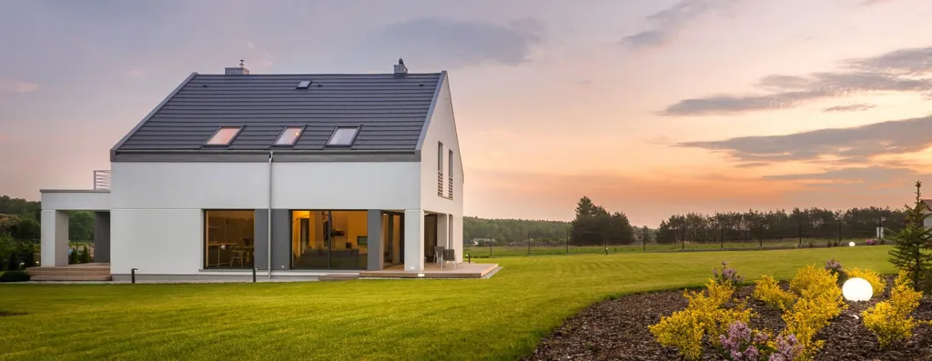 Modernes weißes Einfamilienhaus mit großen Fenstern bei Sonnenuntergang und grünem Rasen