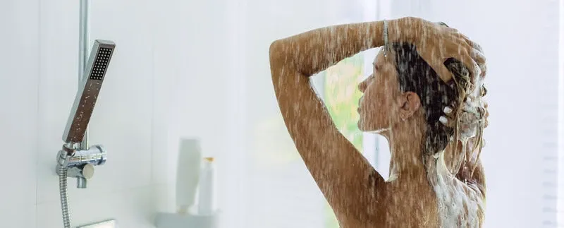 Frau wäscht ihre Haare unter fließendem Wasser in einer hellen Dusche