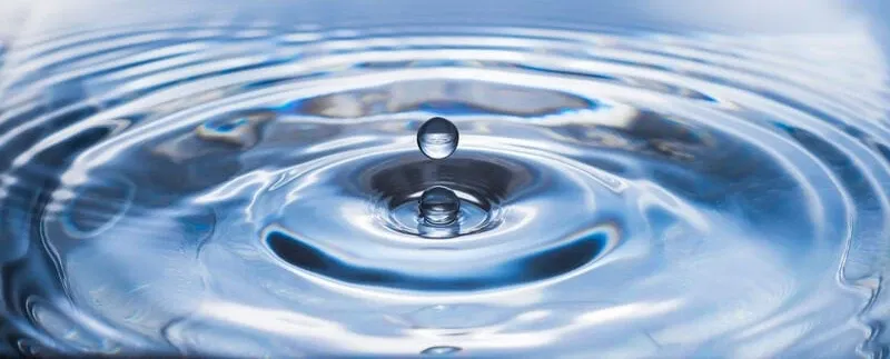 Wassertropfen erzeugt konzentrische Kreise auf blauer spiegelnder Wasseroberfläche