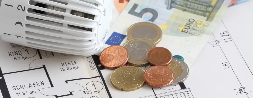 Thermostatventil mit Euro-Geldscheinen und Münzen auf Bauplan als Symbol für Heizungsförderung