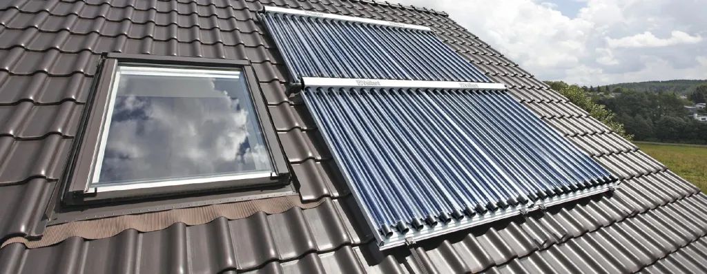Solarthermie-Roehrenkollektoren auf einem Hausdach mit dunklen Ziegeln, daneben ein Dachfenster