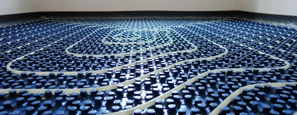 Fußbodenheizungsrohre in Schneckenverlegung auf blauer Noppenplatte während der Installation