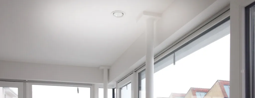 Weiße Zimmerdecke mit rundem Lüftungsventil und Lüftungskanälen in hellem Wohnraum