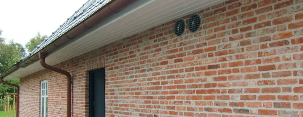 Backsteinhaus mit rundem Außenluft-Ventil für dezentrale Wohnraumlüftung an der Fassade