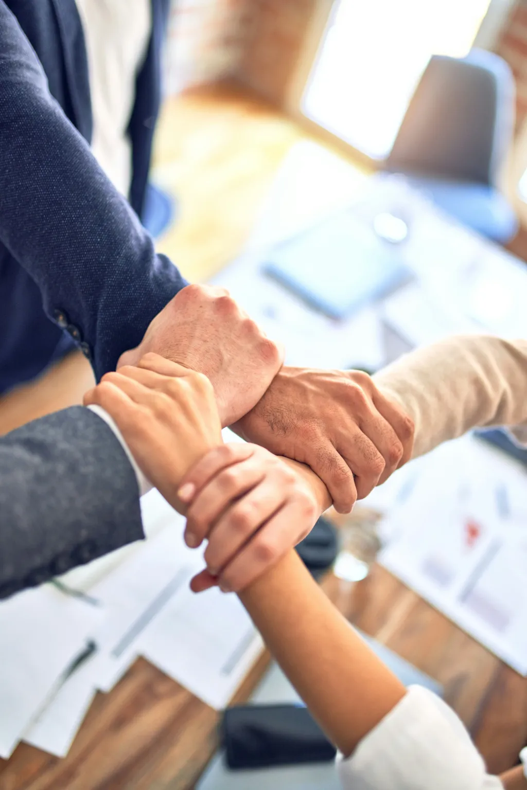 Vier Hände greifen im Kreis ineinander als Symbol für Teamwork und Partnerschaft
